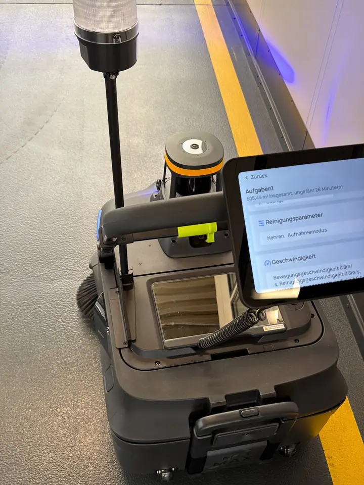 Pudu MT1 Max Kehrroboter von oben im Einsatz in einer Halle, Tablet zeigt Reinigungsaufgabe Kehren im Aufnahmemodus, gelbe Bodenmarkierung